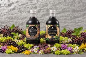 Cuvée 2025 and Cuvée 2026 elderberry bottles on a stone ledge with berries and herbs