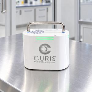 CURIS EnviroPod compact hydrogen peroxide monitoring device with green LED status indicator, sitting on a stainless steel surface in a cleanroom environment