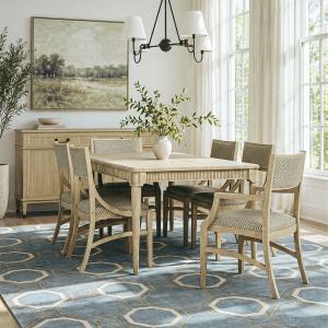 Light wood Stickley Valmont dining table and upholstered chairs in a bright dining room, with a coordinating sideboard, blue geometric rug, and large windows.