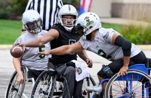 A Los Angeles Raiders wheelchair football player tries to get the ball across the line while two Irving Outlaws players stop him
