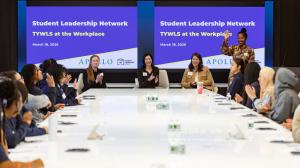 Adults and students dressed in professional clothes are seated around a conference table