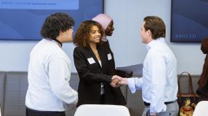 College student shakes hands with an Apollo employee, while another student stands to the side and talks with them