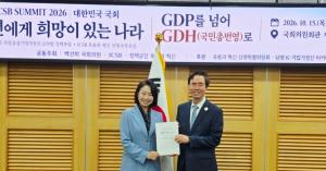 Professor Ki-Chan Kim and Representative Baek Sun-hee hold a report beneath a "Beyond GDP to GDH" banner at Korea's National Assembly.