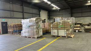 Wrapped and strapped goods on wooden pallets inside a warehouse, with stacked pallets and cartons nearby.