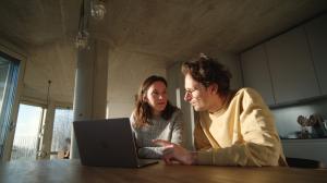 Couple at a kitchen table with a laptop, setting up their household help on Clino
