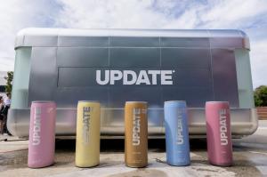 Five giant UPDATE cans in front of the long side of the Nomad Luxe Walk-In L, wrapped in silver with a large UPDATE logo