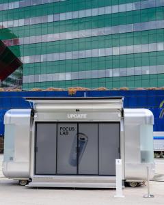 The Nomad Luxe Walk-In L with Focus Lab on its sliding doors and the gullwing canopy raised, outside the Pacific Design Center