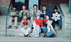  Shekinah Grace Moyes and seven fellow performers sit on outdoor stone steps, holding red and white flowers and a large white snowflake decoration.