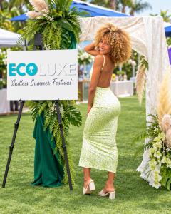 Woman in a floral dress poses beside the ECOLUXE Endless Summer Festival sign at the 2026 pre-Emmys luxury lounge in Beverly Hills, California.
