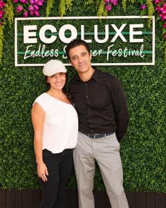 Gilles Marini and Carol Marini pose together in front of the ECOLUXE Endless Summer Festival backdrop at the 2026 pre-Emmys event in Beverly Hills.