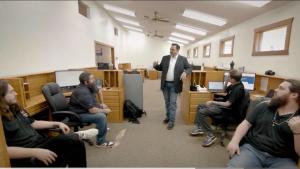 Quick Strike Media team members meeting in the agency’s Palestine, Texas office, with one standing team member addressing four colleagues seated at their desks.