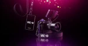 A professional video camera and a VRE7 TV press credential badge on a dark cinematic background, representing the independent entertainment network's red-carpet and premiere event coverage.