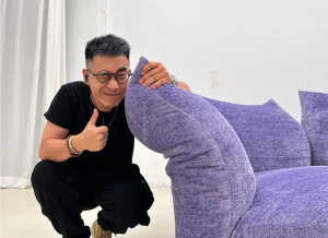 Customer giving a thumbs up beside a purple upholstered sofa at a furniture sourcing visit in Foshan