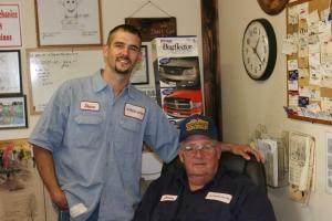 Shane Price standing beside his father, James Price, in the office of their auto repair shop in Palestine, Texas.