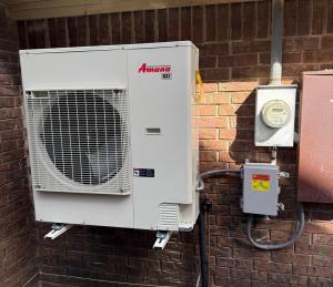 Amana R32 outdoor HVAC unit with an All Around Comfort Heat & Air decal, mounted on brackets against gray vinyl siding in Cabot, Arkansas