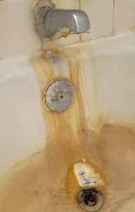 White bathtub with orange iron stains running from the faucet and overflow plate to the drain