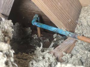 Heavily corroded copper water pipe with blue-green buildup running through wet attic insulation in a Brazoria County, Texas home
