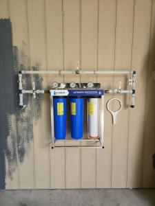 Three-stage whole-house water filtration system with pressure gauges and bypass valves mounted on a wall in a new Brazoria County, Texas home