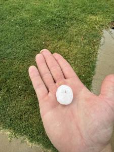 Large hailstone held in a hand above a grass lawn after a hailstorm in Cabot, Arkansas