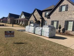 Pallets of new shingles and roofing materials on a driveway beside a brick home in Cabot, Arkansas, with a J. Cole Construction yard sign
