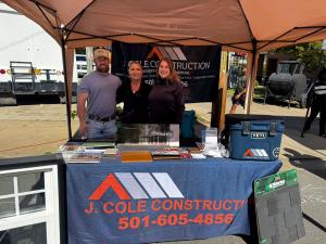 J. Cole Construction team members at an outdoor event booth with roofing shingle samples, siding samples, and a company banner