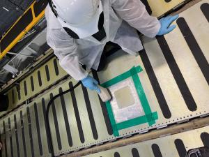 A technician wearing protective clothing and a hard hat applies localized surface treatment to a green-taped repair area on a C-5 Galaxy cargo floor at Westover Air Reserve Base.