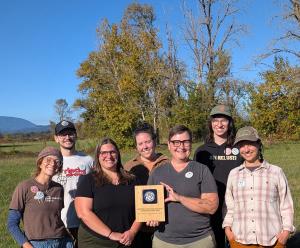 Seven individuals standing in a field holding an award plaque