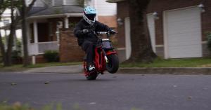 Helmeted rider lifting the front wheel of a red FRP Moto M3 electric mini bike