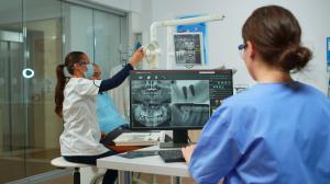 Dental assistant reviewing the dental imaging scans on a monitor while the dentist adjusts the imaging machine