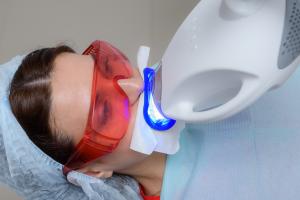 Woman wears protective glasses while receiving professional teeth whitening treatment at a dental clinic