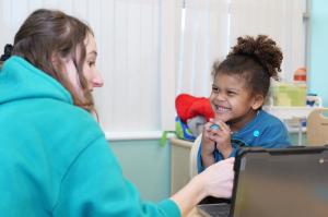 A young boy with curly hair grins widely at a Bierman team member during a one-on-one session at a table with a laptop.