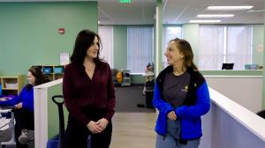 Two Bierman team members talk while walking through a center with green walls and open workspaces.