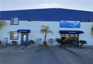 Commercial storefront painted in crisp white and bold blue with blue entry awnings, potted plants, and parking stalls