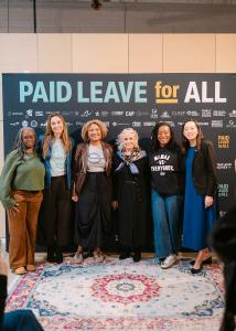 Six women stand smiling in front of a step and repeat that says "Paid Leave for All."
