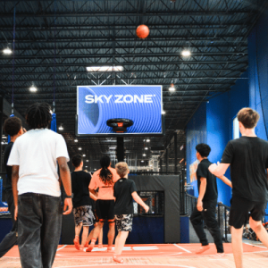 People gather in a Sky Zone trampoline park beneath a large illuminated sign.