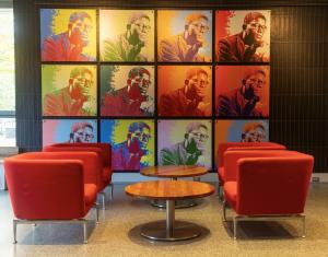 A colorful wall of repeating portraits of artist Richard Hunt with red chairs and tables in a dining setting.