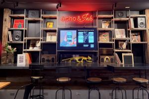 a bookcase with vinyl records and record players on display with a bright red neon sign, "Echo & Ink"; stools sit in front of the countertop