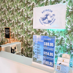 Reception counter with tropical leaf wallpaper, “The Refresh” spa sign, massage membership plans, and a $69.95 offer.