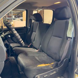 A worn front seat with torn upholstery exposing the yellow cushioning underneath.