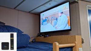 A flat-screen TV playing a broadcast mounted above a blue bunk bed inside a maritime vessel for offshore oil rigs. The FMUSER FBE013 IPTV set-top box is visible below the screen, ensuring stable entertainment.