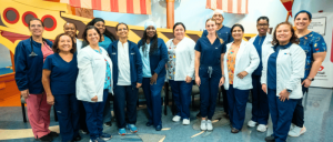 Group of healthcare professionals posing together in a colorful hospital or clinic hallway.