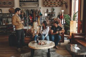 Four friends enjoy glasses of red wine at Picayune Cellars in Calistoga, relaxing around a rustic wooden table with a charcuterie platter in a cozy tasting room featuring Southwestern-style textiles, clothing displays and leather seating.