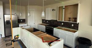 Kitchen remodel in progress, with new white cabinets installed and a laser level marking lines for the island