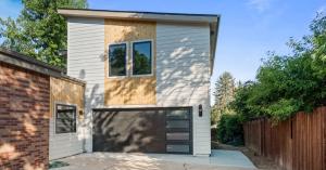 Two-story ADU with white and natural wood siding, a dark garage door below and two windows above