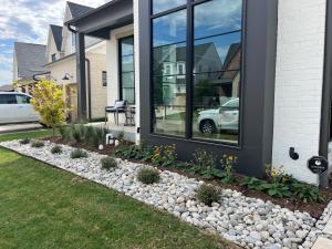 Front yard landscape bed in Richardson, TX with black-eyed Susans, ornamental grasses, a small tree, fresh mulch and a river rock border along the lawn