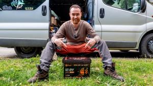 Eine Person mit einer Lithink Batterie vor einem Campervan; Motiv von der Website zu Lithink Care+.