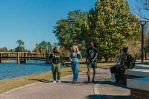 A group of students walking alongside a lake with two students sitting nearby.