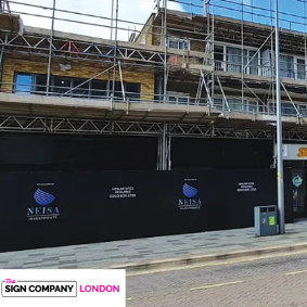 Black printed construction hoarding panels installed along a scaffolded building site