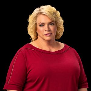 Janelle Brown, star of TLC’s Sister Wives, poses against a solid black background wearing a deep red blouse and gold hoop earrings, with shoulder-length blonde hair and a confident expression.