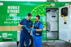 Two KFSH emergency staff reviewing a tablet beside a green mobile stroke unit vehicle in Riyadh